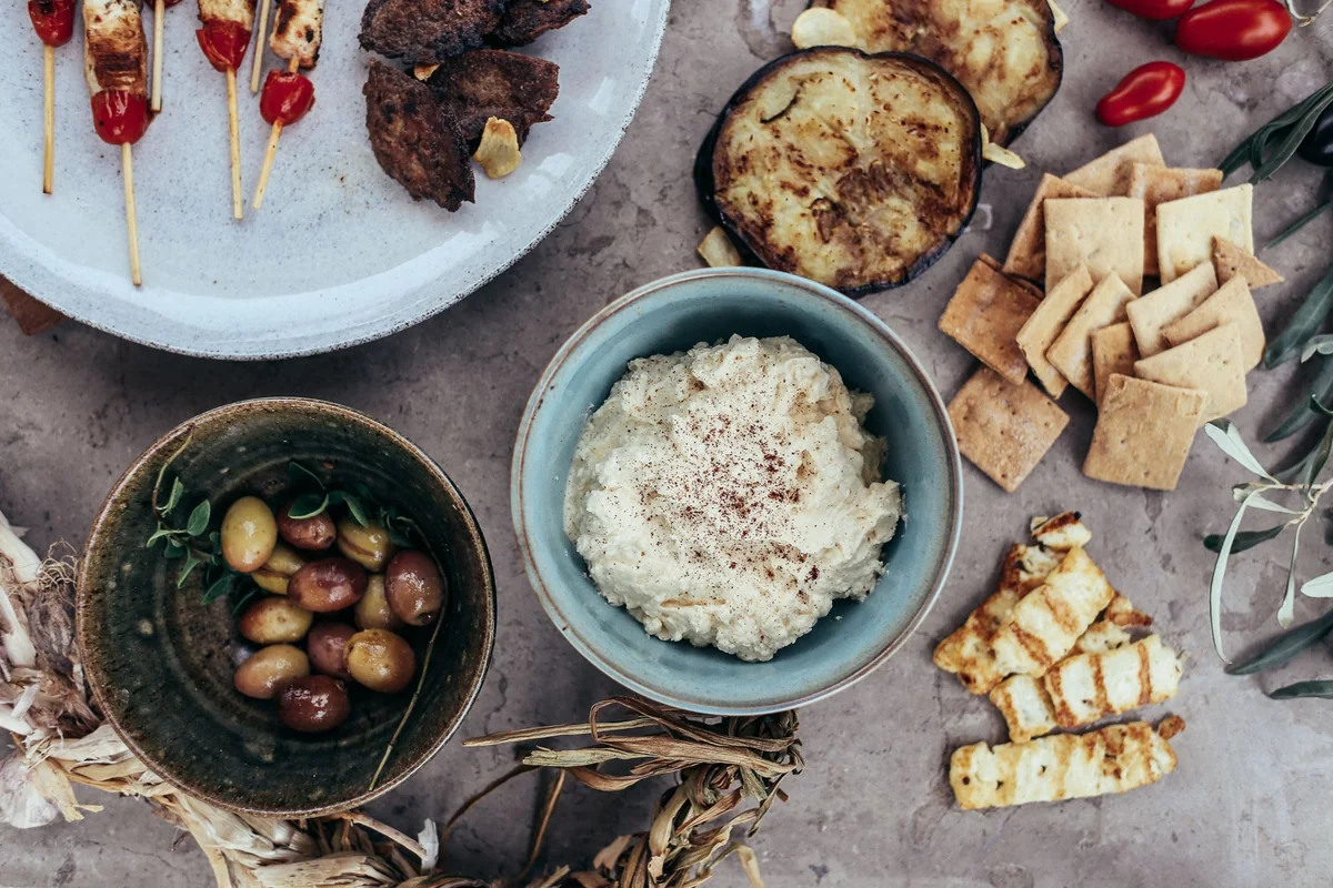 An overhead spread of grilled skewers, olives, dip and grilled vegetables — representative of Greek taverna food, not the actual three courses served