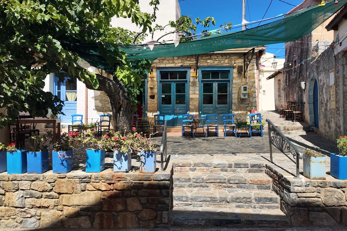 A stone taverna with painted blue chairs, a shade awning and string lights — representative of a traditional Greek taverna, not the actual venue